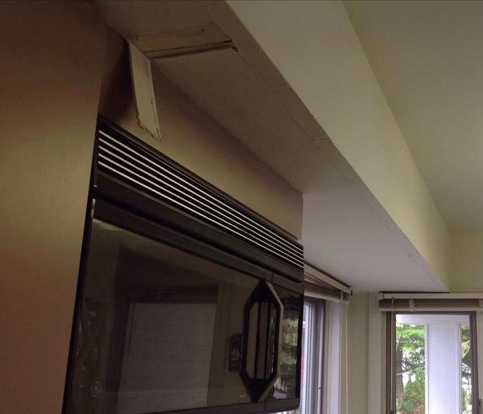 A water damaged piece of drywall hangs detached from the ceiling above the microwave