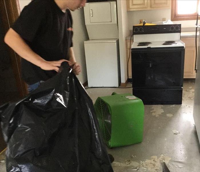 male with black garbage bag in kitchen with appliances and drying unit
