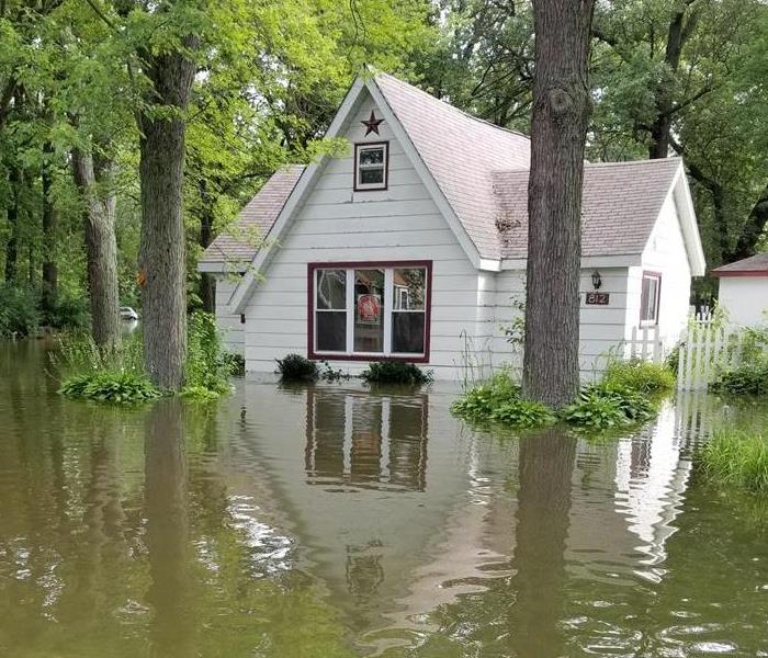 Water surrounds the property of a Wisconsin home. Trees bases and grass submerged in water.